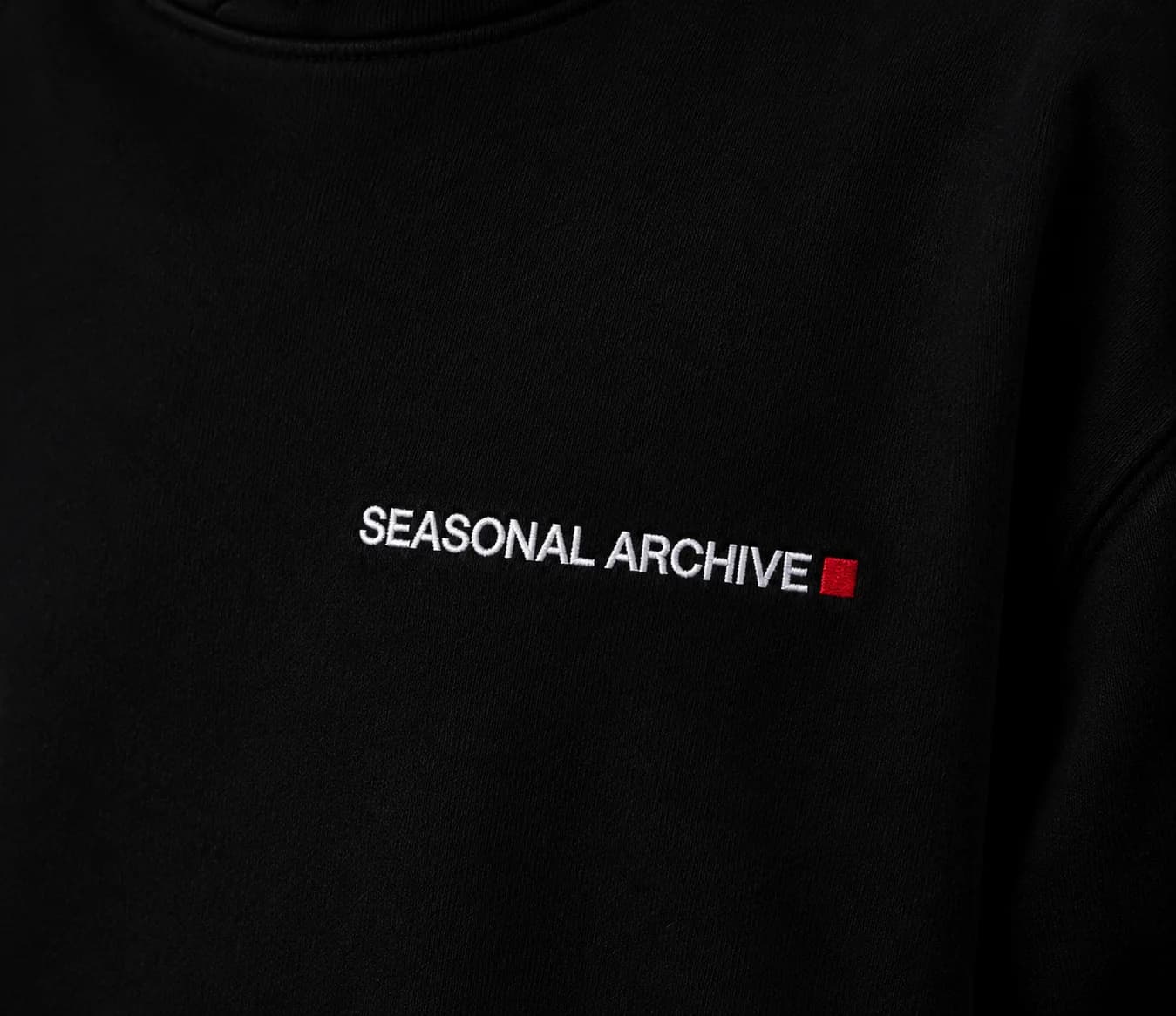 Close on the embroidered wordmark: SEASONAL ARCHIVE in white thread, ending in one red square.